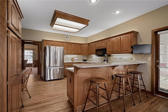 kitchen featuring stainless steel refrigerator, backsplash, a kitchen bar, light hardwood / wood-style floors, and kitchen peninsula