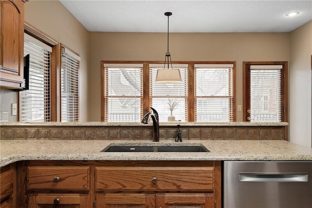 kitchen with light stone countertops, sink, stainless steel dishwasher, and decorative light fixtures