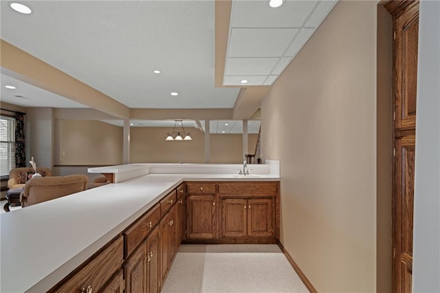 kitchen with decorative light fixtures, kitchen peninsula, sink, and light carpet