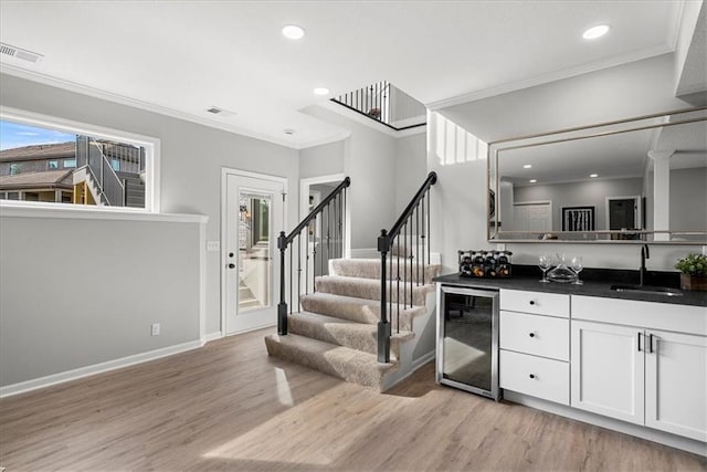 interior space featuring white cabinetry, sink, beverage cooler, ornamental molding, and light hardwood / wood-style flooring