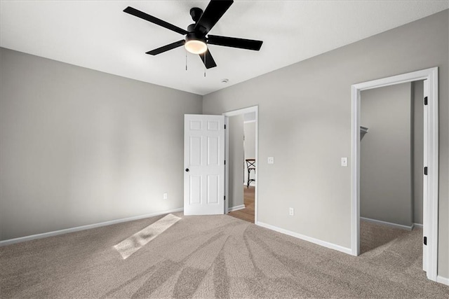 unfurnished bedroom with a walk in closet, light colored carpet, a closet, and ceiling fan