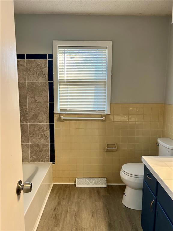 full bathroom with toilet, vanity, tile walls, wood-type flooring, and tub / shower combination