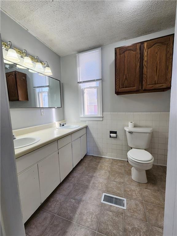 bathroom featuring toilet, a textured ceiling, tile patterned flooring, tile walls, and vanity