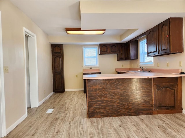 kitchen with light hardwood / wood-style floors, a wealth of natural light, kitchen peninsula, and dark brown cabinetry