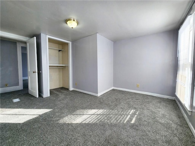 unfurnished bedroom with a closet, dark carpet, and multiple windows