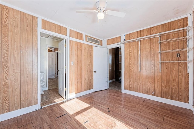 unfurnished bedroom with ceiling fan, wood walls, wood-type flooring, connected bathroom, and a closet