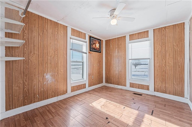 empty room featuring ceiling fan, hardwood / wood-style floors, crown molding, and wood walls