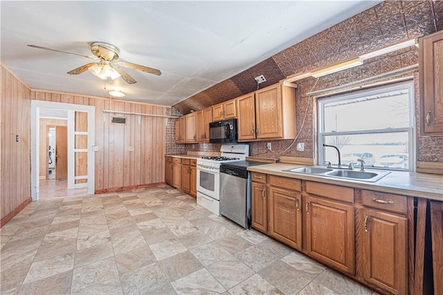 kitchen with sink, white range with gas stovetop, stainless steel dishwasher, wooden walls, and ceiling fan