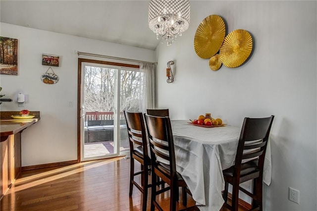 dining space with an inviting chandelier, wood-type flooring, and vaulted ceiling