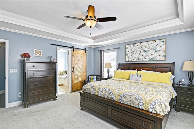 carpeted bedroom with ceiling fan, a barn door, a raised ceiling, and ensuite bath