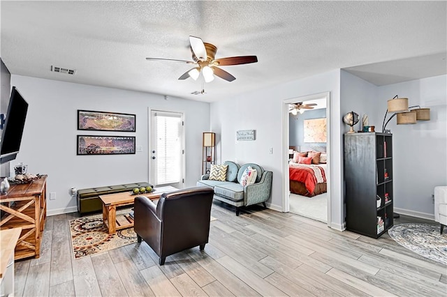 living room with ceiling fan, a textured ceiling, and light hardwood / wood-style flooring