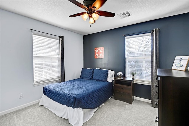 bedroom featuring ceiling fan, light colored carpet, a textured ceiling, and multiple windows