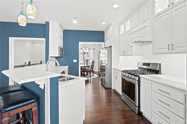 kitchen with decorative light fixtures, backsplash, white cabinetry, light stone countertops, and stainless steel appliances