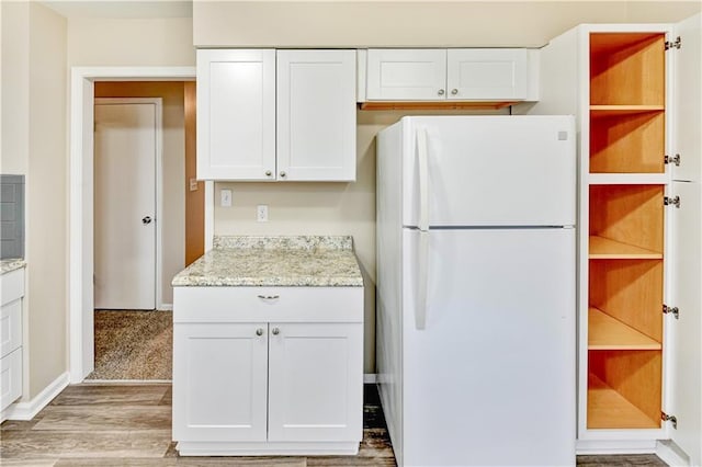 kitchen featuring white fridge, light stone countertops, light hardwood / wood-style flooring, and white cabinetry