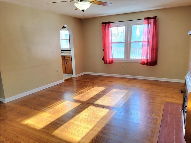 empty room with baseboards, arched walkways, and wood finished floors