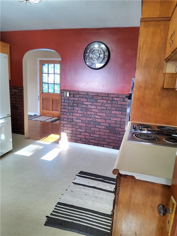 kitchen with white refrigerator, stainless steel gas stovetop, and brick wall