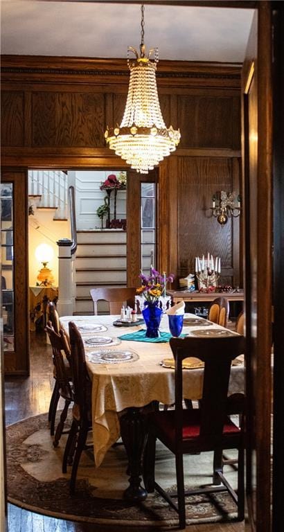 dining space with hardwood / wood-style floors, a chandelier, and wooden walls