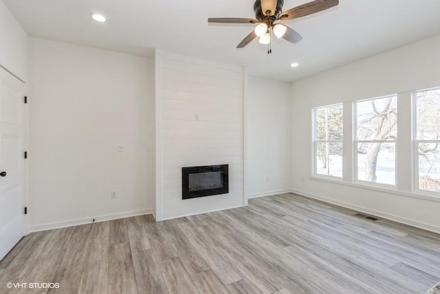 unfurnished living room with a large fireplace, ceiling fan, and light hardwood / wood-style floors