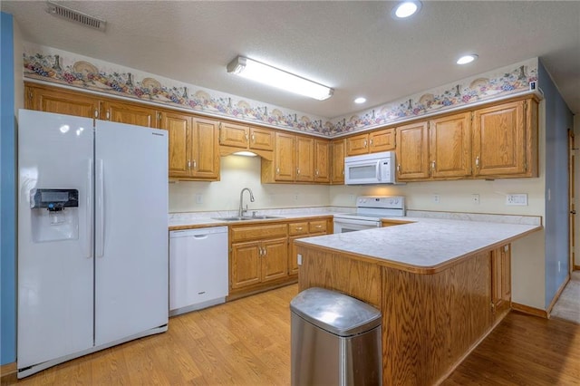 kitchen featuring sink, a breakfast bar area, white appliances, kitchen peninsula, and light wood-type flooring