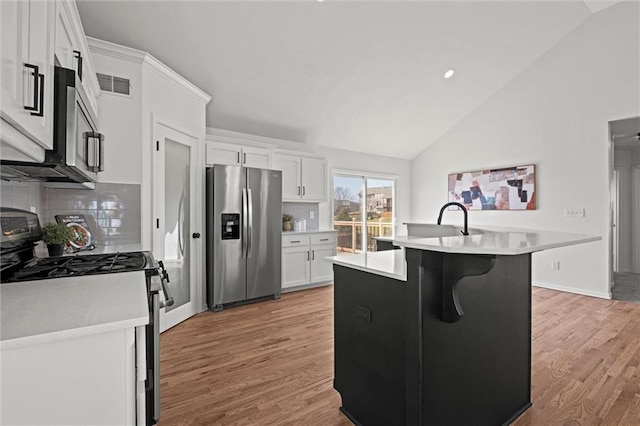 kitchen with vaulted ceiling, white cabinetry, stainless steel appliances, and light countertops