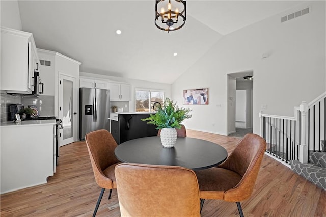 dining area featuring high vaulted ceiling, light wood finished floors, visible vents, stairway, and a chandelier