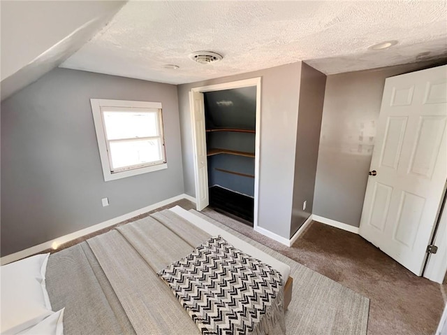 interior space featuring a textured ceiling, vaulted ceiling, a closet, carpet flooring, and a walk in closet