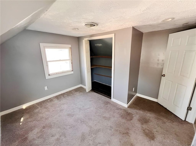 unfurnished bedroom featuring lofted ceiling, a textured ceiling, dark colored carpet, and a closet