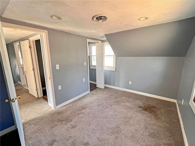 additional living space with a textured ceiling, vaulted ceiling, and carpet flooring