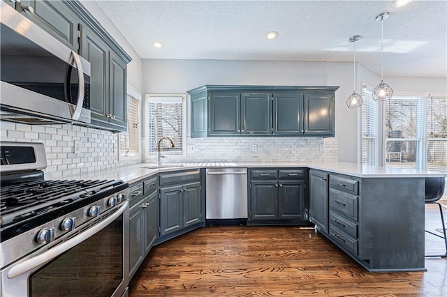 kitchen featuring kitchen peninsula, hanging light fixtures, appliances with stainless steel finishes, a kitchen bar, and dark hardwood / wood-style floors