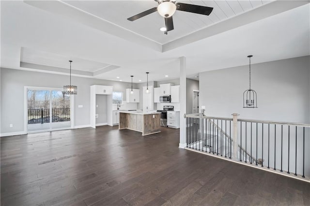 unfurnished living room with ceiling fan with notable chandelier, a raised ceiling, sink, and dark hardwood / wood-style floors