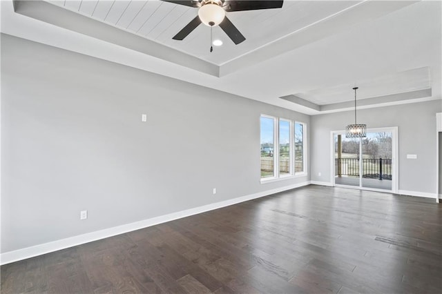 empty room with ceiling fan with notable chandelier, a tray ceiling, and dark hardwood / wood-style flooring