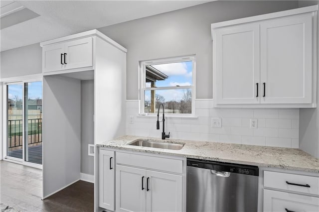 kitchen featuring light stone counters, white cabinets, stainless steel dishwasher, and sink