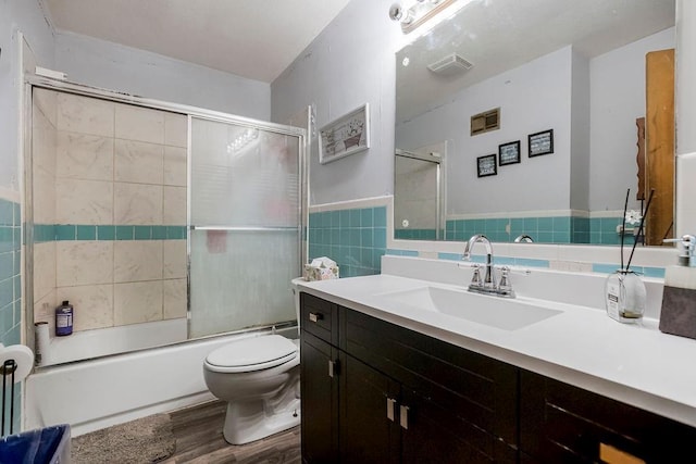 full bathroom featuring toilet, bath / shower combo with glass door, tile walls, vanity, and hardwood / wood-style flooring