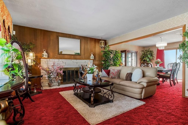 living room featuring wood walls, carpet flooring, a stone fireplace, a textured ceiling, and a chandelier