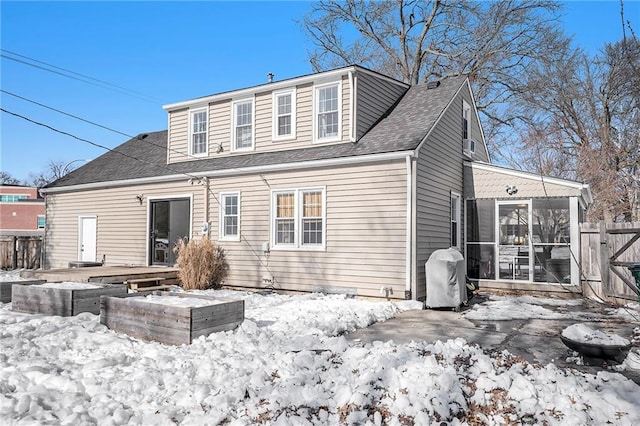 snow covered back of property featuring a sunroom