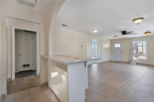 kitchen featuring a kitchen bar, ceiling fan, light tile patterned floors, and kitchen peninsula