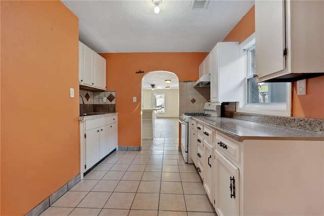 kitchen featuring light tile patterned floors, white gas stove, backsplash, white cabinetry, and sink