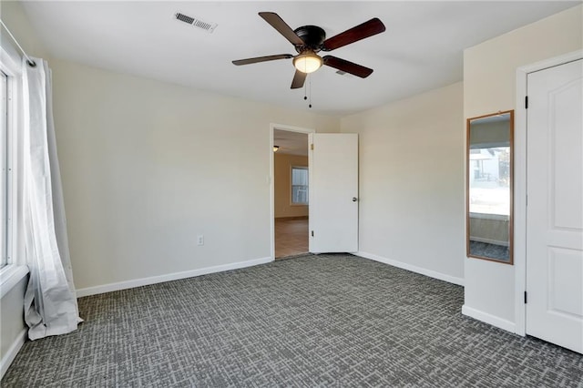 spare room featuring ceiling fan and dark carpet