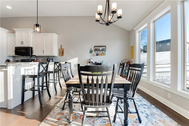 dining area featuring dark wood-type flooring, a healthy amount of sunlight, vaulted ceiling, and a notable chandelier