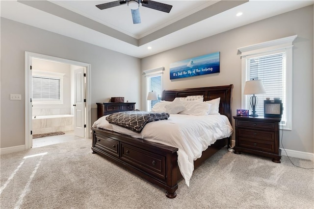 bedroom featuring ceiling fan, light colored carpet, ensuite bath, and a tray ceiling