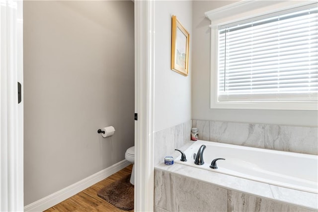 bathroom with hardwood / wood-style flooring, tiled tub, and toilet