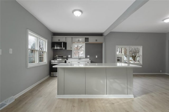 kitchen featuring gray cabinetry, stainless steel appliances, light hardwood / wood-style flooring, and a center island