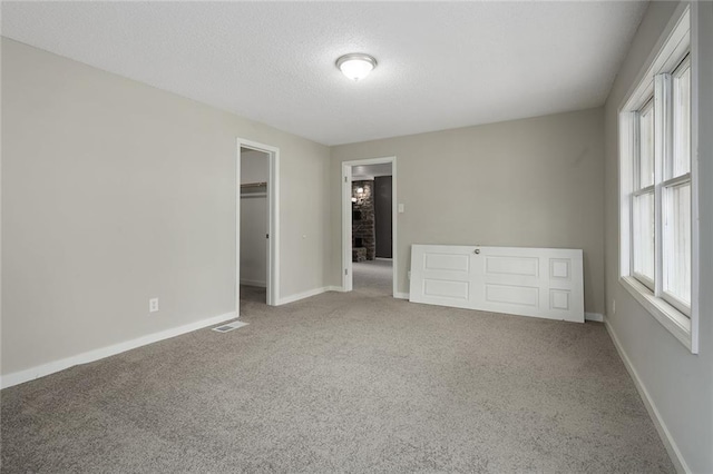 unfurnished bedroom with a walk in closet, a closet, multiple windows, and carpet