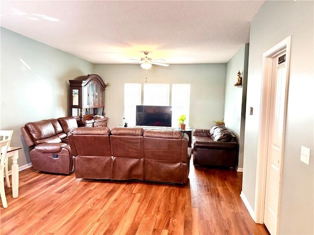 living room with a textured ceiling, ceiling fan, and wood-type flooring