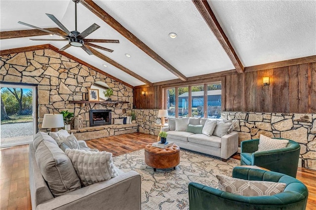 living room featuring light hardwood / wood-style floors, vaulted ceiling with beams, a fireplace, and a textured ceiling