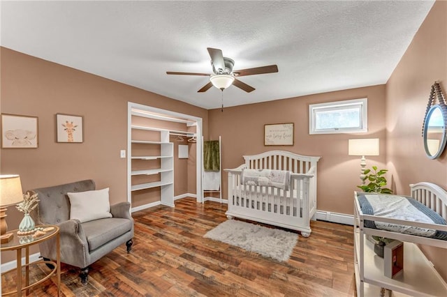 bedroom featuring ceiling fan, wood-type flooring, a closet, a crib, and a baseboard radiator