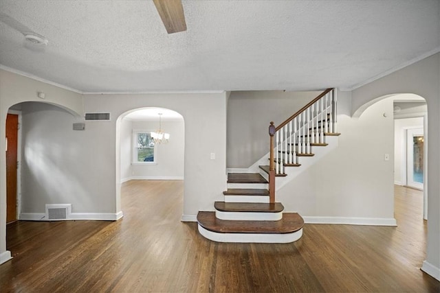 staircase featuring a textured ceiling, hardwood / wood-style floors, crown molding, and a chandelier