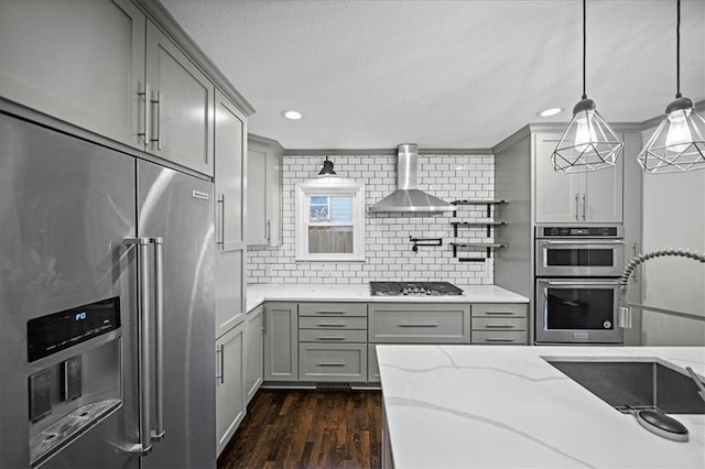 kitchen featuring gray cabinets, stainless steel appliances, pendant lighting, wall chimney range hood, and backsplash