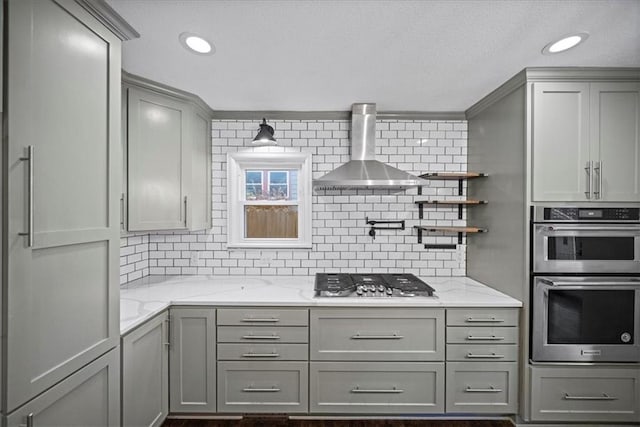 kitchen with stainless steel appliances, wall chimney range hood, gray cabinetry, and light stone countertops