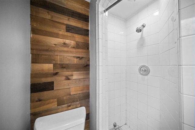 bathroom with tiled shower, wood walls, and toilet